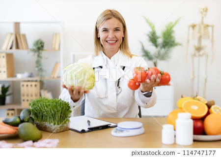 Mature female doctor nutritionist holds fresh organic tomatoes and cabbage. Mature female doctor nutritionist holds fresh organic tomatoes and cabbage. 114747177