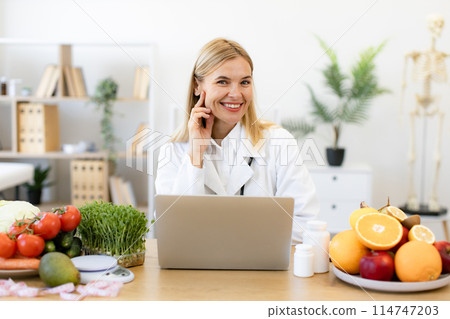 Nutritionist working on laptop and writing diet plan for patient. 114747203