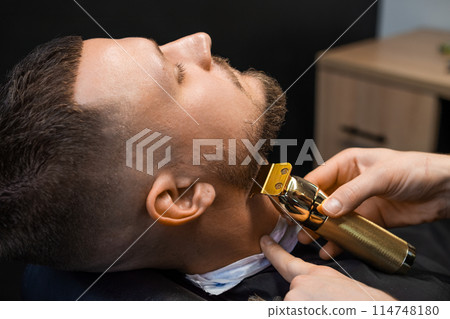 Barber shearing beard to man in barbershop, close up. Barber shearing beard to man in barbershop, close up. 114748180
