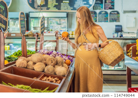 A pregnant woman is at a fruit stand in a grocery store Pregnant woman buying organic vegetables and fruits at Mexican style farmers market 114749044