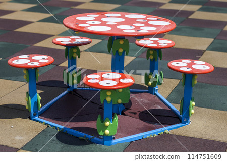 Close-up shot of bright colorful new round child small table and five stools outdoors on square rubber flooring on kindergarten playground. Place for games, rest and recreation. Close-up shot of bright colorful new round child small table and five stools outdoors on square rubber flooring on kindergarten playground. Place for games, rest and recreation. 114751609