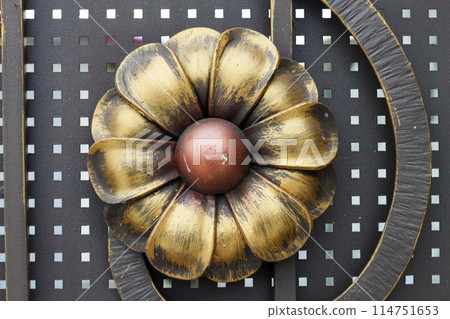Close-up detail of beautiful vintage forged metal big yellow and red flower decorating iron gray fence, gate or door. Work of blacksmith, protection, art and fantasy concept. Close-up detail of beautiful vintage forged metal big yellow and red flower decorating iron gray fence, gate or door. Work of blacksmith, protection, art and fantasy concept. 114751653