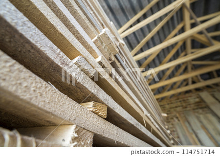 Neatly piled long stack of wooden boards inside attic room under construction. Neatly piled long stack of wooden boards inside attic room under construction. 114751714