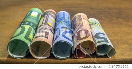 Five, ten, twenty, fifty and one hundred euro rolled bills banknotes on wooden table background. 114751961