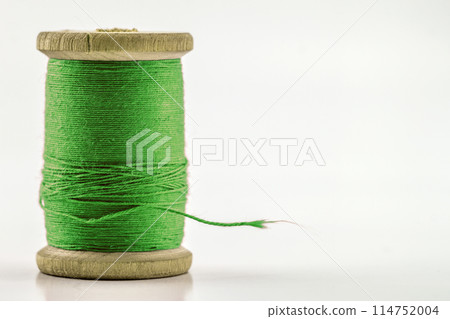Reel or spool of green sewing thread isolated on white. Shallow depth of field. Close-up macro shot. 114752004