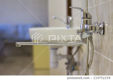 Water tap, chrome stainless metal faucet connected to shower stall tiled wall, mixer cold hot water on blurred bathroom background. Modern home interior. 114752259