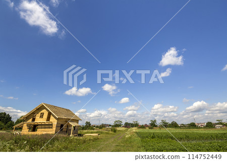 New wooden ecological not finished cottage from natural materials under construction in green field on distant village and blue sky copy space background. Old traditions and modern building concept. 114752449