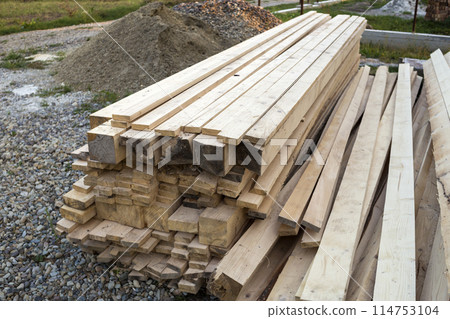 Stack of natural brown uneven rough wooden boards on building site. Industrial timber for carpentry, building, repairing and furniture, lumber material for roofing construction. 114753104