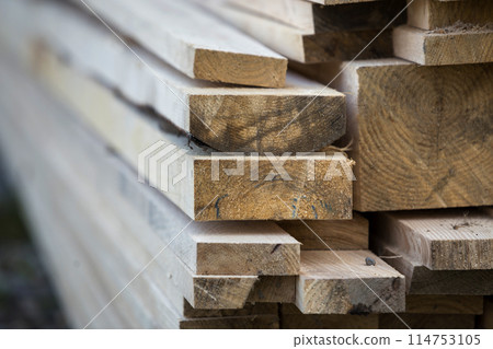 Close-up of piled stack of natural brown uneven rough wooden boards lit by bright sun. Industrial timber for carpentry, building, repairing and furniture, lumber material for construction. 114753105