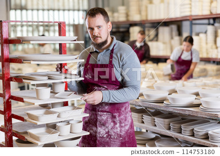 Young man posing at rack with ceramic dishes 114753180