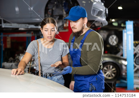 Unsatisfied young girl touching surface of her car standing next to male car mechanic 114753184