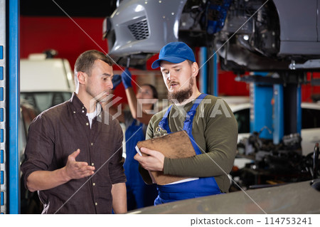 Mechanic guy signs agreement with young man client Mechanic guy signs agreement with young man client 114753241