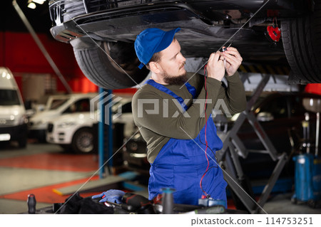 Auto mechanic diagnoses an engine using a measuring device in car service center 114753251