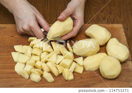 Woman's hand with a knife cutting slicing potatoes on wooden board in kitchen. Healthy eating and lifestyle. View from above close-up Woman's hand with a knife cutting slicing potatoes on wooden board in kitchen. Healthy eating and lifestyle. View from above close-up 114753271