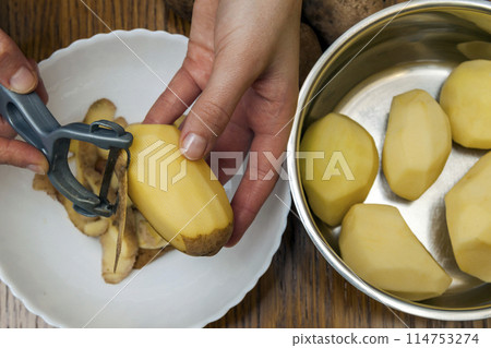 Detail of woman hands peeling fresh yellow potato with kitchen peeler, Food preparation concept. Detail of woman hands peeling fresh yellow potato with kitchen peeler, Food preparation concept. 114753274