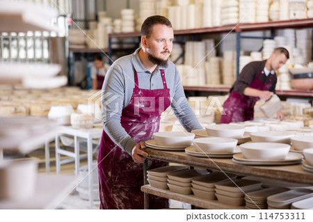 Young man moves rack with ceramic blanks Young man moves rack with ceramic blanks 114753311