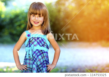 Outdoor portrait of optimistic smiling pretty little girl in blue dress 114753325