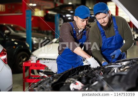 Two mechanic guys repairing under hood of car 114753359