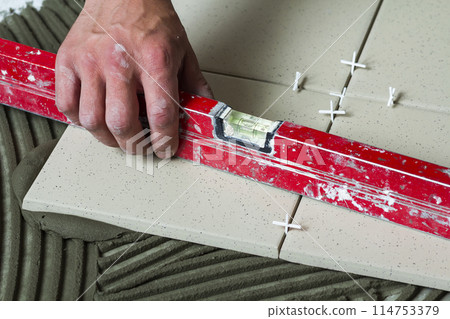 Ceramic tiles and tools for tiler. Worker hand installing floor tiles. Home improvement, renovation - ceramic tile floor adhesive, mortar, level. Ceramic tiles and tools for tiler. Worker hand installing floor tiles. Home improvement, renovation - ceramic tile floor adhesive, mortar, level. 114753379