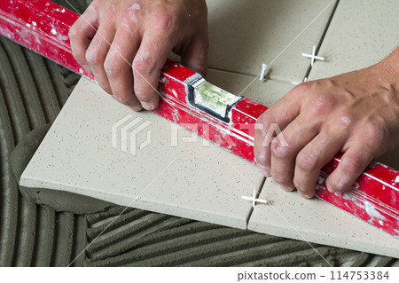 Ceramic tiles and tools for tiler. Worker hand installing floor tiles. Home improvement, renovation - ceramic tile floor adhesive, mortar, level. 114753384