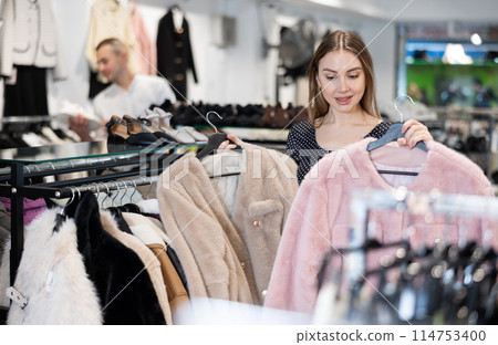Young woman choosing fur coat in clothing store Young woman choosing fur coat in clothing store 114753400