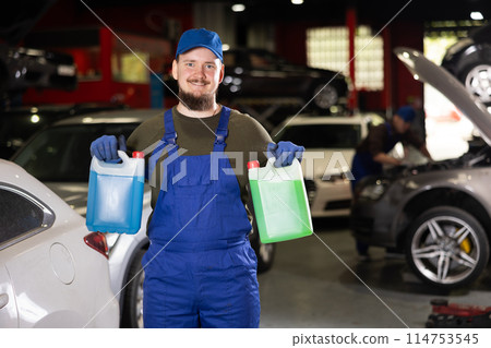 Portrait of professional auto mechanic in uniform with canisters of blue and red antifreeze in his hands 114753545