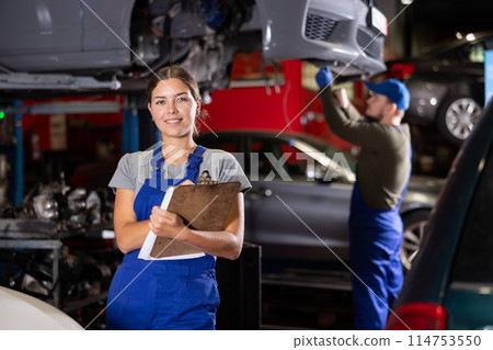 Female car service worker keeps records of work performed by auto mechanics in car service station - makes notes on paper 114753550
