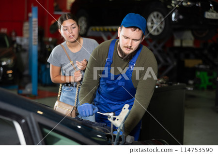 Young guy mechanic fixing woman client's car 114753590