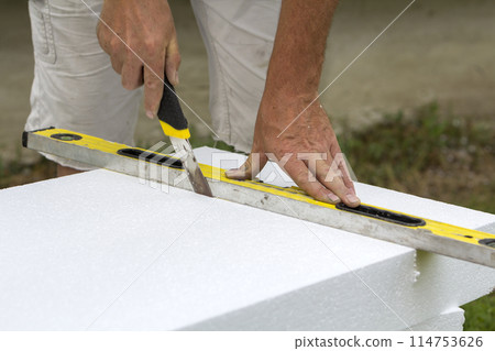 Close-up of worker hand with knife and level cutting white rigid polyurethane foam sheet for house insulation. Modern technology, renovation, professional job, alternative for mineral wool concept. 114753626
