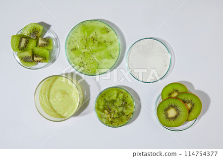 White table containing plenty glassware with fresh kiwi and organic exfoliation cream has kiwi origin. Creative photo from top view with blank space for adding text or elements of design 114754377