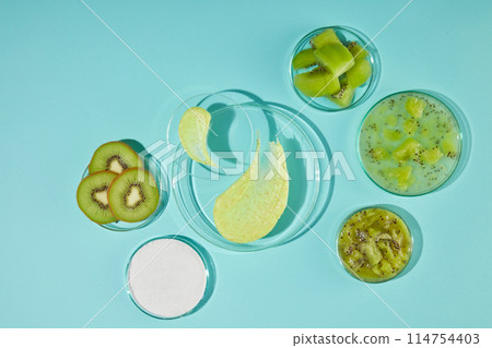 Blank glass pedestals with smudge of yellow exfoliation cream displayed in center of pastel blue table top with some glass dishes of fresh kiwi ingredient placed around. Displaying space, top view Blank glass pedestals with smudge of yellow exfoliation cream displayed in center of pastel blue table top with some glass dishes of fresh kiwi ingredient placed around. Displaying space, top view 114754403
