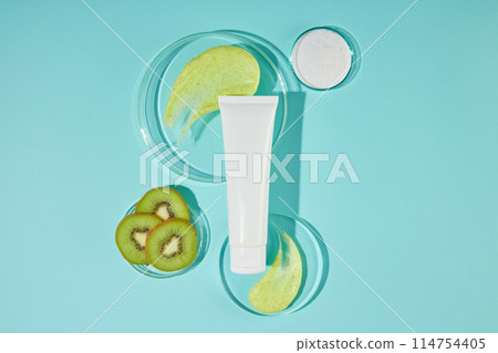 Mock up for promote with a sample cosmetic tube displayed between two glass platforms, next to a dish of fresh kiwi. Scrubs of kiwi helps skin increase elasticity, firmness, and shine 114754405