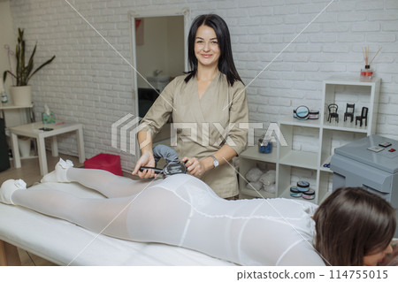 Woman in special white suit getting anti cellulite massage in a spa salon. LPG, and body contouring treatment in clinic.Reset body weight with LPG massage Woman in special white suit getting anti cellulite massage in a spa salon. LPG, and body contouring treatment in clinic.Reset body weight with LPG massage 114755015