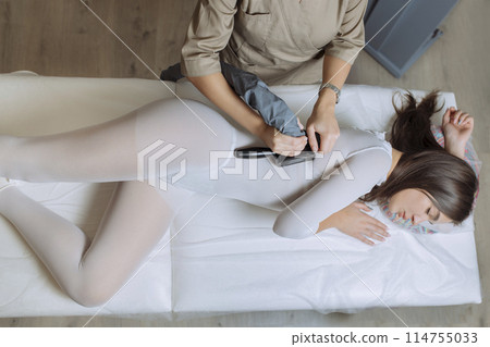 Woman in special white suit getting anti cellulite massage in a spa salon. LPG, and body contouring treatment in clinic.Reset body weight with LPG massage Woman in special white suit getting anti cellulite massage in a spa salon. LPG, and body contouring treatment in clinic.Reset body weight with LPG massage 114755033