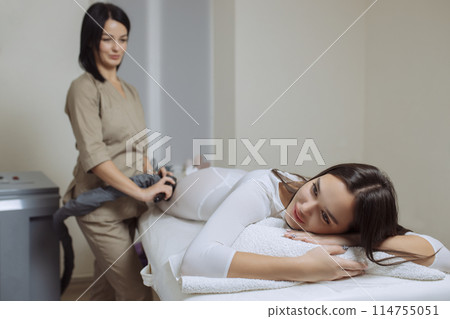 Woman in special white suit getting anti cellulite massage in a spa salon. LPG, and body contouring treatment in clinic.Reset body weight with LPG massage 114755051