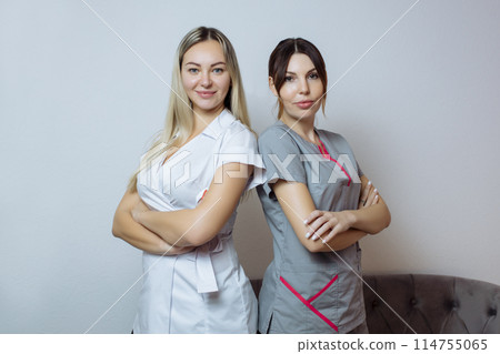 Two young beautiful sexy women cosmetologists colleagues in white stylish clothing standing and smiling. Two young beautiful sexy women cosmetologists colleagues in white stylish clothing standing and smiling. 114755065