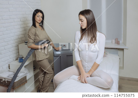 Woman in special white suit getting anti cellulite massage in a spa salon. LPG, and body contouring treatment in clinic.Reset body weight with LPG massage Woman in special white suit getting anti cellulite massage in a spa salon. LPG, and body contouring treatment in clinic.Reset body weight with LPG massage 114755075