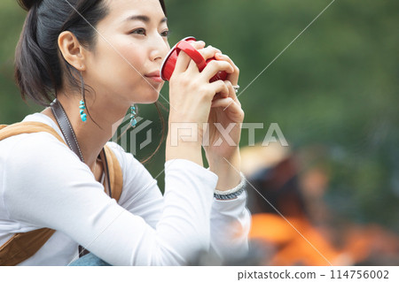 Woman drinking coffee beside a campfire Woman drinking coffee beside a campfire 114756002