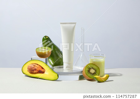 Advertising photo on white background was shot from front, a glass podium containing a blank cosmetic tube next to a glass beaker of yellow cream, fresh avocado and kiwi. Blank space for design Advertising photo on white background was shot from front, a glass podium containing a blank cosmetic tube next to a glass beaker of yellow cream, fresh avocado and kiwi. Blank space for design 114757287