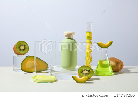 Cosmetic or beauty care product advertising which has avocado and kiwi origin, a green bottle without label placed on glass podium, fresh kiwi, avocado and lab items decorated. Front view, copy space 114757290