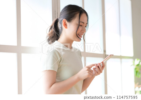 年輕女子站在窗邊看著她的智慧型手機 114757595