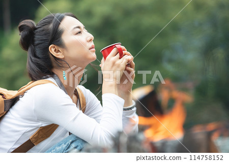 Woman drinking coffee beside a campfire 114758152