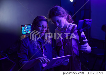 Portrait of female video production crew working together in dark purple light 114758771