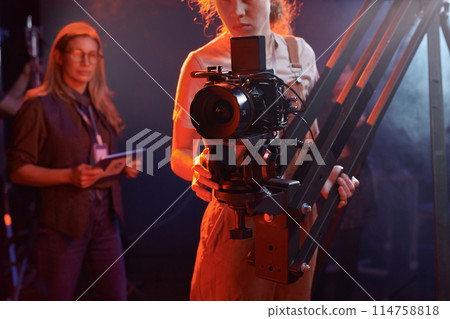 Cropped shot of young woman operating video camera on rig in studio with neon lights copy space 114758818