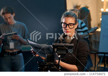 Waist up portrait of female director looking at camera screen while leading video production on set Waist up portrait of female director looking at camera screen while leading video production on set 114758872