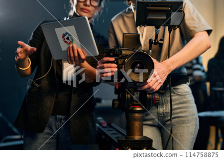 Font view cropped shot of two women operating pro video camera working in film crew on set Font view cropped shot of two women operating pro video camera working in film crew on set 114758875