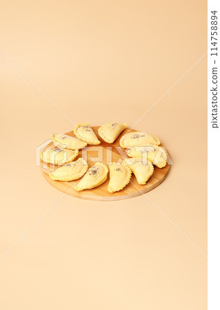 Raw samosas on a wooden round board. Traditional Central Asian cuisine, frozen semi-finished products, copy space. 114758894