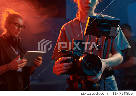 Cropped shot of female cameraman operating equipment in studio set with neon lights copy space Cropped shot of female cameraman operating equipment in studio set with neon lights copy space 114758899