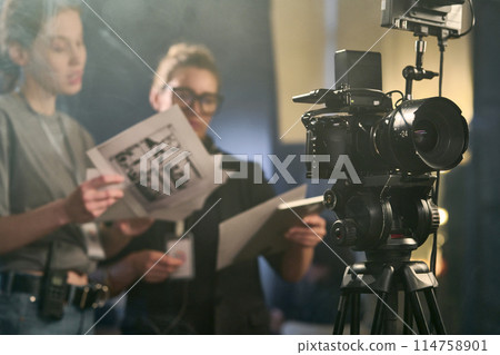 Professional digital video camera on stand at production studio or movie recording with crew working in background copy space Professional digital video camera on stand at production studio or movie recording with crew working in background copy space 114758901