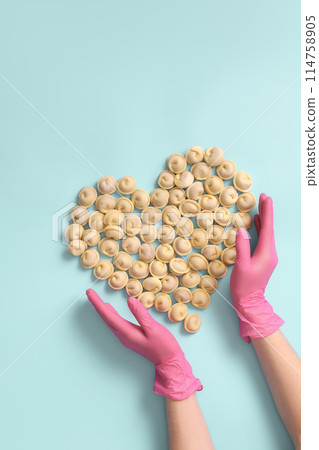 Top view chef's hands in rubber gloves lay out semi-finished raw dumplings in the shape of a heart, love for his job as a cook, copy space. Top view chef's hands in rubber gloves lay out semi-finished raw dumplings in the shape of a heart, love for his job as a cook, copy space. 114758905
